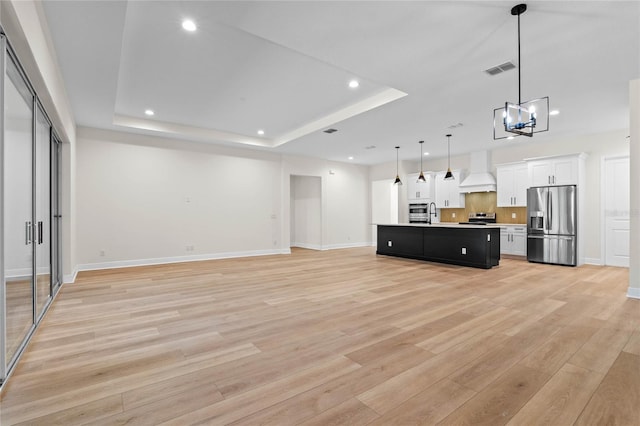 kitchen featuring custom range hood, open floor plan, appliances with stainless steel finishes, and a raised ceiling