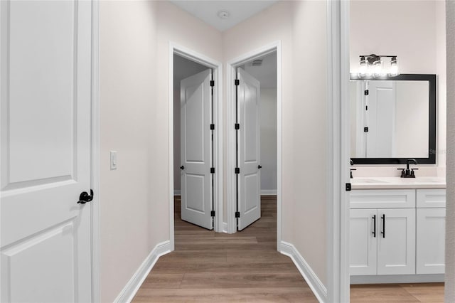 hallway featuring light wood-style flooring, baseboards, a sink, and visible vents