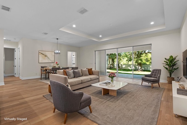 living room featuring visible vents, light wood-type flooring, a tray ceiling, and recessed lighting