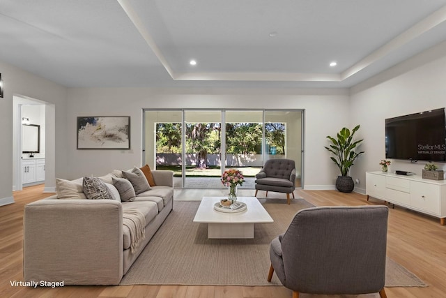 living room featuring a tray ceiling, light wood-style floors, baseboards, and recessed lighting
