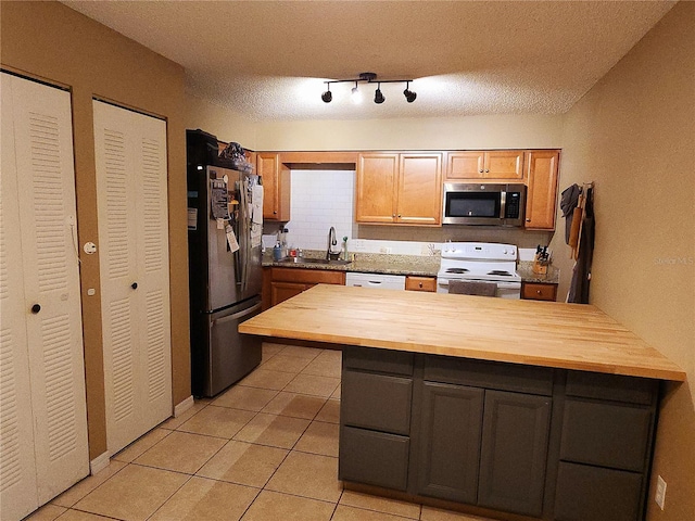 kitchen featuring sink, a textured ceiling, appliances with stainless steel finishes, light tile patterned flooring, and butcher block counters