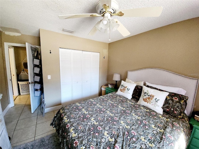 bedroom with ceiling fan, a closet, light tile patterned floors, and a textured ceiling