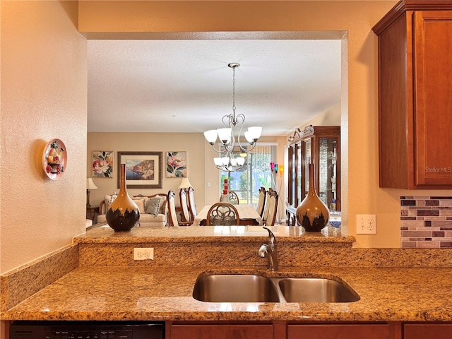 kitchen featuring sink, hanging light fixtures, dishwashing machine, light stone counters, and a chandelier