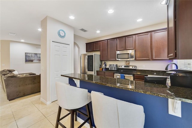 kitchen featuring a kitchen bar, light tile patterned floors, appliances with stainless steel finishes, and dark stone counters