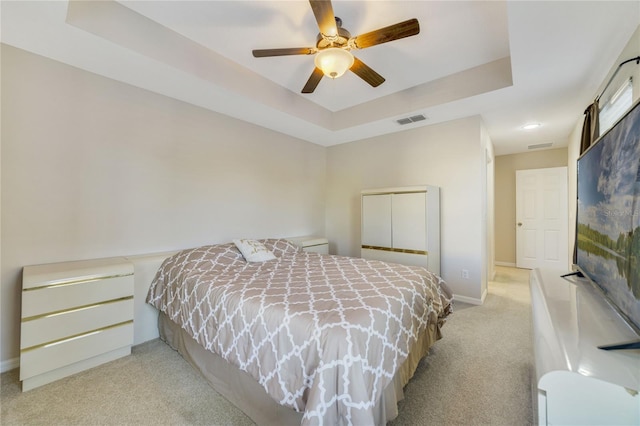 carpeted bedroom featuring a tray ceiling and ceiling fan