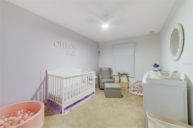 carpeted bedroom featuring ceiling fan and a nursery area