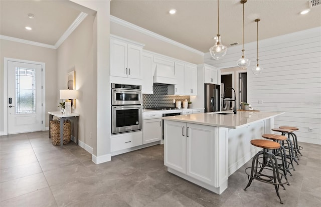 kitchen with sink, stainless steel appliances, decorative light fixtures, a kitchen island with sink, and white cabinets