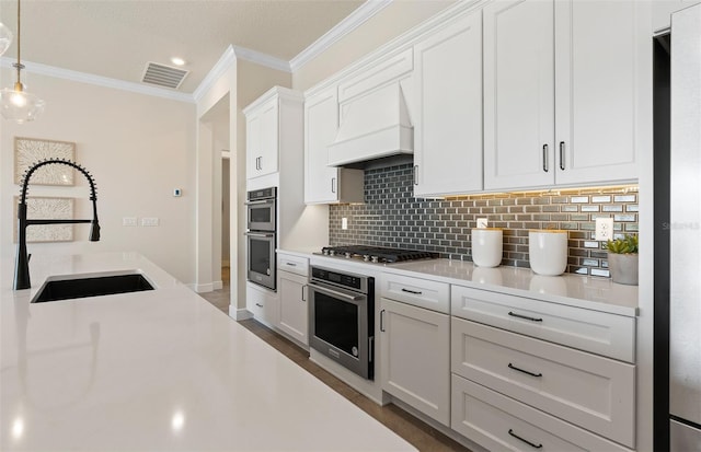 kitchen with sink, pendant lighting, white cabinets, custom range hood, and appliances with stainless steel finishes