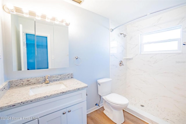 bathroom featuring hardwood / wood-style flooring, vanity, toilet, and tiled shower