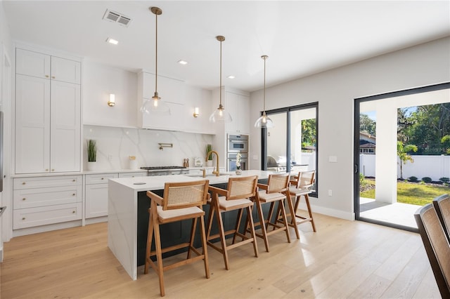 kitchen featuring white cabinets, an island with sink, and pendant lighting