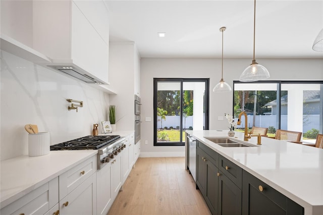 kitchen featuring pendant lighting, white cabinets, sink, light wood-type flooring, and appliances with stainless steel finishes