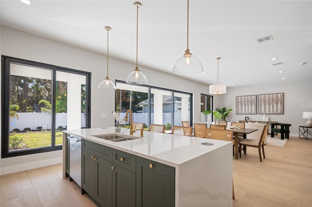 kitchen featuring dishwasher, sink, light hardwood / wood-style flooring, pendant lighting, and a center island with sink