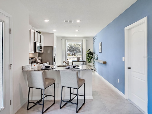 kitchen featuring light stone counters, kitchen peninsula, a breakfast bar area, light tile patterned floors, and appliances with stainless steel finishes