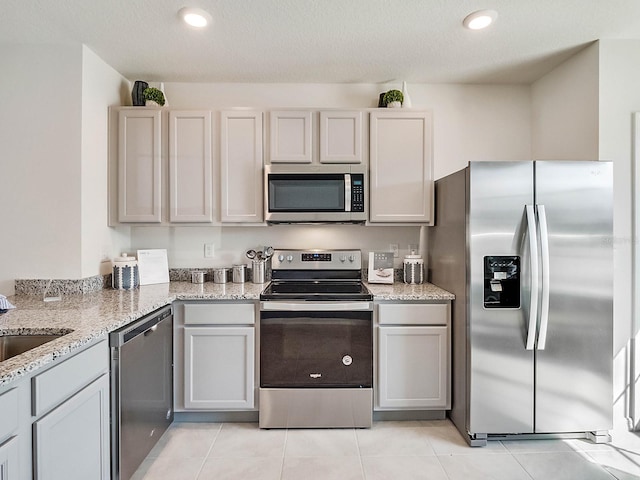 kitchen featuring gray cabinetry, light stone counters, a textured ceiling, light tile patterned floors, and appliances with stainless steel finishes