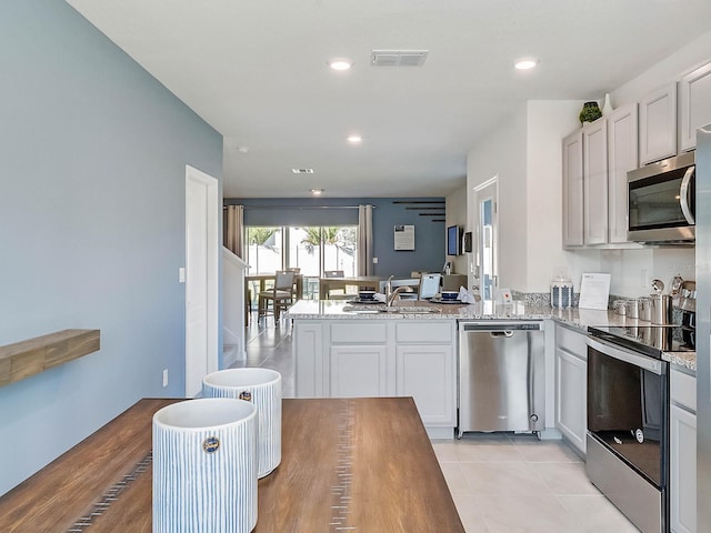 kitchen featuring light stone countertops, stainless steel appliances, kitchen peninsula, and sink