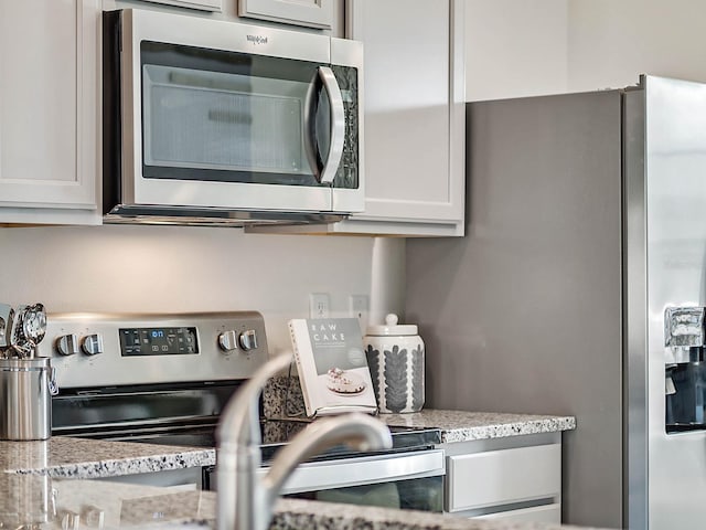 kitchen with light stone countertops, white cabinetry, and stainless steel appliances