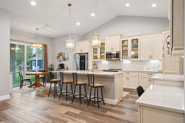 kitchen with light hardwood / wood-style flooring, an island with sink, appliances with stainless steel finishes, and vaulted ceiling