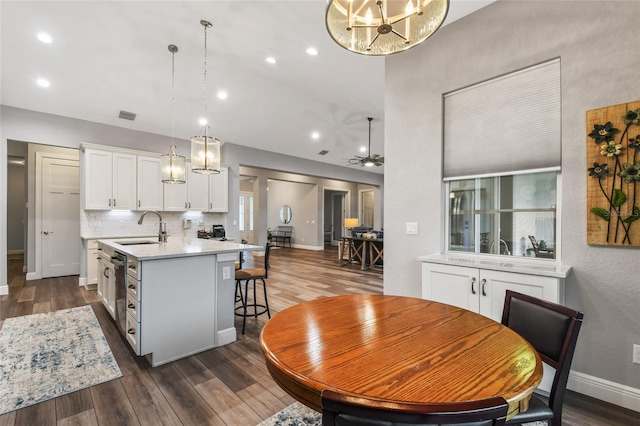 kitchen with a center island with sink, sink, hanging light fixtures, dark hardwood / wood-style flooring, and white cabinetry