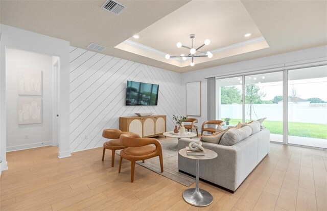 living room with a tray ceiling, wooden walls, crown molding, a notable chandelier, and light hardwood / wood-style floors