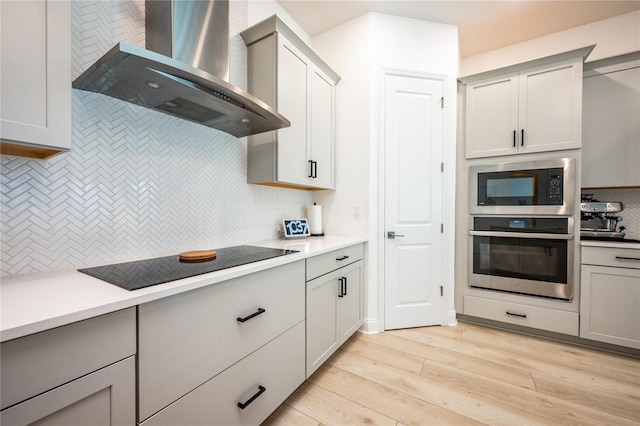 kitchen featuring backsplash, wall chimney exhaust hood, stainless steel appliances, light hardwood / wood-style flooring, and gray cabinets