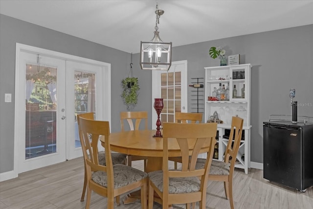 dining space with an inviting chandelier, light wood-type flooring, and french doors