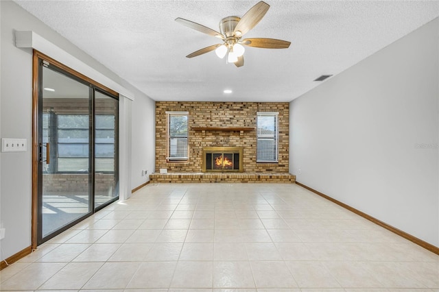 unfurnished living room featuring ceiling fan, light tile patterned floors, a textured ceiling, and a brick fireplace