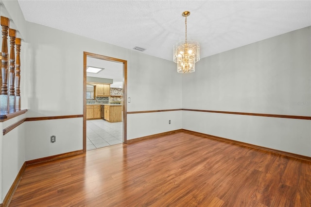 spare room with a chandelier, light hardwood / wood-style floors, and a textured ceiling