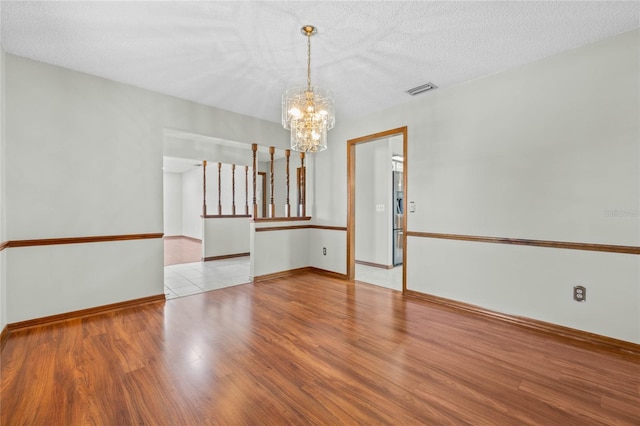 unfurnished room featuring a textured ceiling, light hardwood / wood-style floors, and a notable chandelier