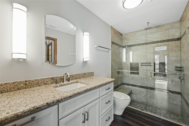 bathroom featuring vanity, hardwood / wood-style flooring, toilet, and a shower with door