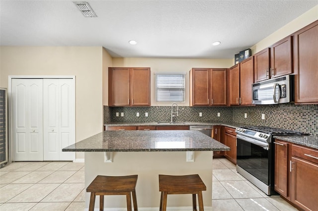 kitchen featuring light tile patterned floors, appliances with stainless steel finishes, a kitchen breakfast bar, and a sink