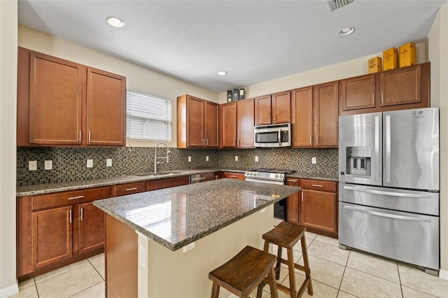 kitchen with stainless steel appliances, a sink, dark stone countertops, and light tile patterned floors