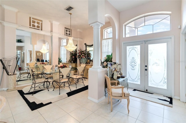 entrance foyer featuring french doors, a towering ceiling, light tile patterned floors, and ornate columns