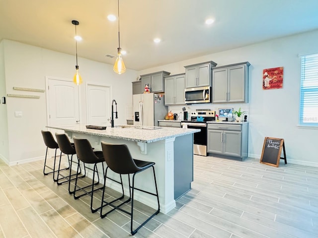 kitchen featuring a kitchen breakfast bar, gray cabinetry, stainless steel appliances, a kitchen island with sink, and decorative light fixtures