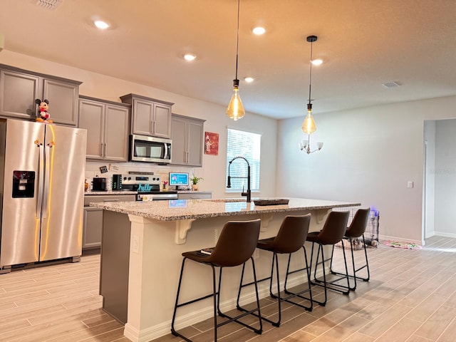 kitchen with stainless steel appliances, light stone counters, pendant lighting, a kitchen bar, and a center island with sink