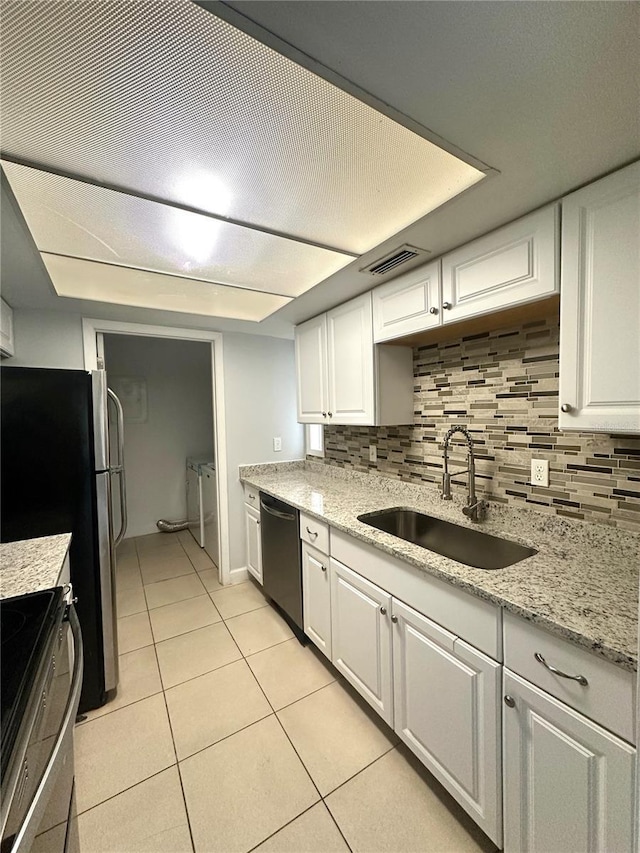 kitchen with visible vents, appliances with stainless steel finishes, washing machine and dryer, white cabinetry, and a sink