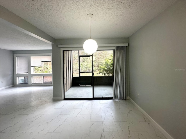 empty room with a textured ceiling, marble finish floor, and baseboards