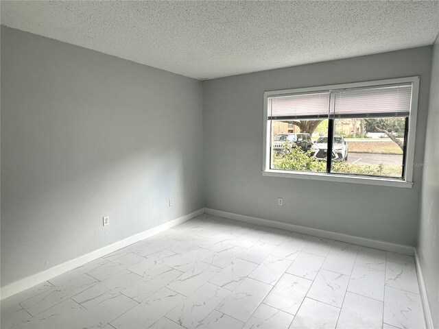 spare room with a textured ceiling, marble finish floor, and baseboards