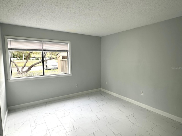 empty room with marble finish floor, baseboards, and a textured ceiling