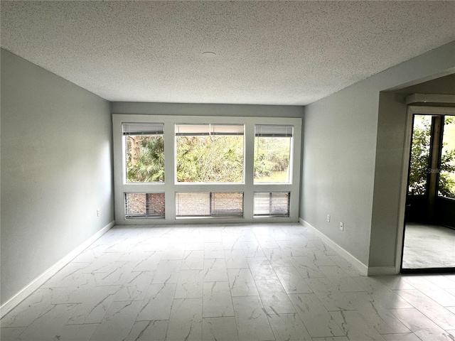 spare room with marble finish floor, a textured ceiling, and baseboards