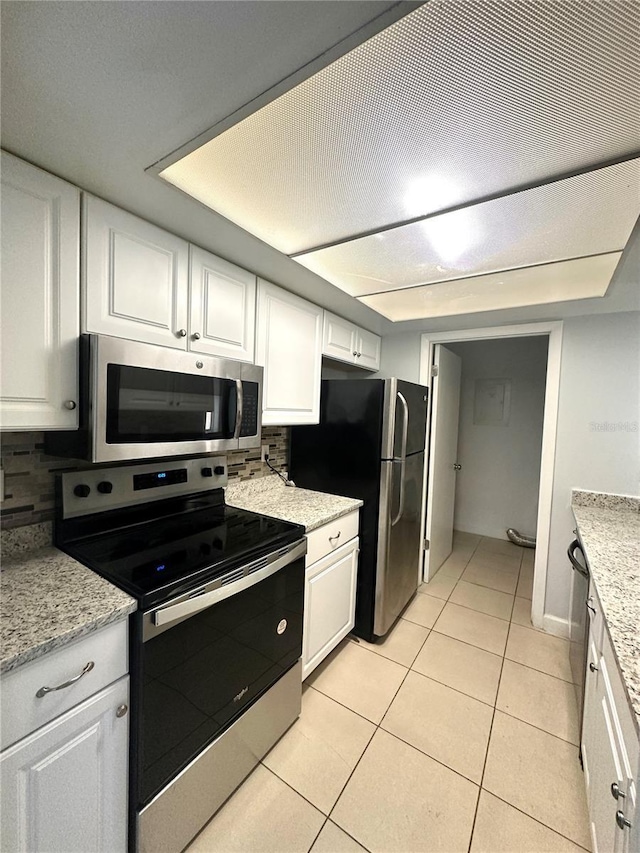 kitchen with light tile patterned floors, tasteful backsplash, appliances with stainless steel finishes, light stone counters, and white cabinetry