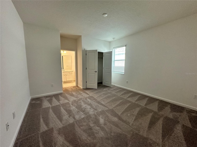 unfurnished bedroom with ensuite bath, carpet floors, a closet, and a textured ceiling