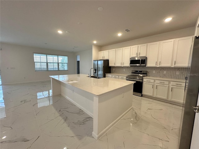 kitchen with white cabinetry, appliances with stainless steel finishes, light stone countertops, and a kitchen island with sink