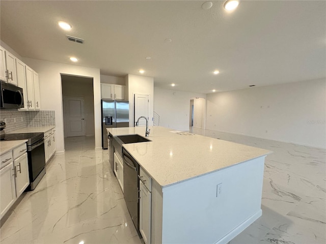 kitchen with light stone countertops, white cabinetry, appliances with stainless steel finishes, and a center island with sink