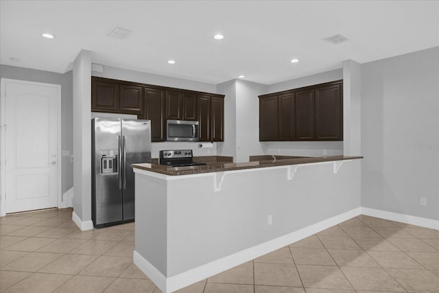 kitchen with a kitchen breakfast bar, kitchen peninsula, light tile patterned floors, and appliances with stainless steel finishes