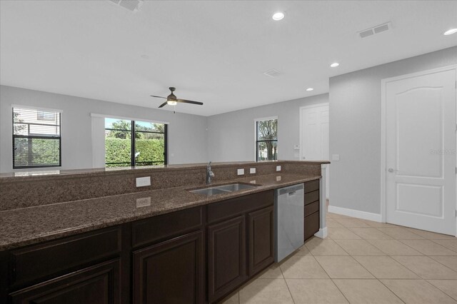 kitchen featuring ceiling fan, sink, light tile patterned floors, dark stone countertops, and dishwasher