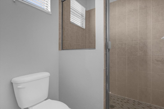 bathroom featuring a shower with shower door and toilet