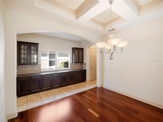 kitchen with coffered ceiling, an inviting chandelier, decorative backsplash, light wood-type flooring, and dark brown cabinets