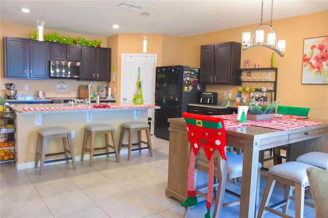 kitchen with a kitchen bar, black fridge, an island with sink, and decorative light fixtures