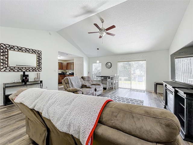 living room with a textured ceiling, ceiling fan, light hardwood / wood-style flooring, and lofted ceiling