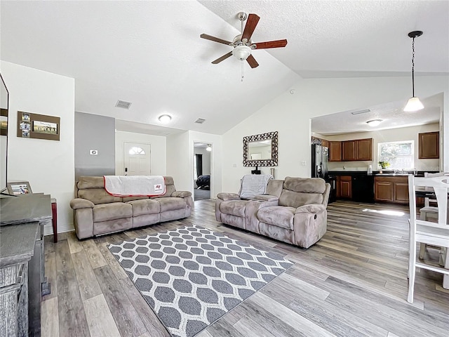 living room with ceiling fan, lofted ceiling, a textured ceiling, and light hardwood / wood-style flooring